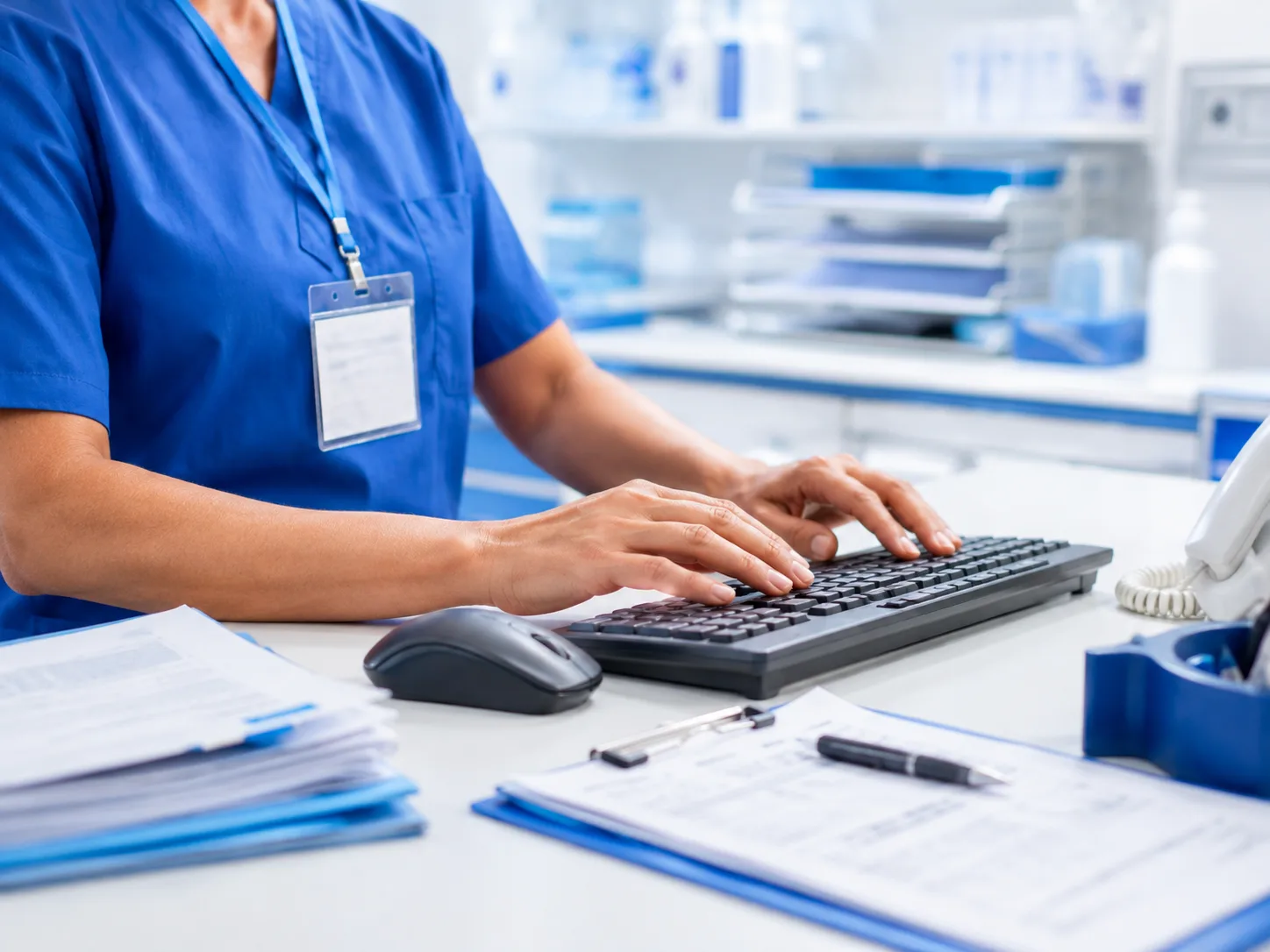 A clinician in scrubs entering patient information at a workstation keyboard